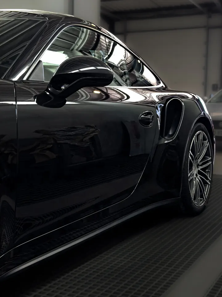 Flanc d'une Porsche noire aux reflets nets, dans un local fermé